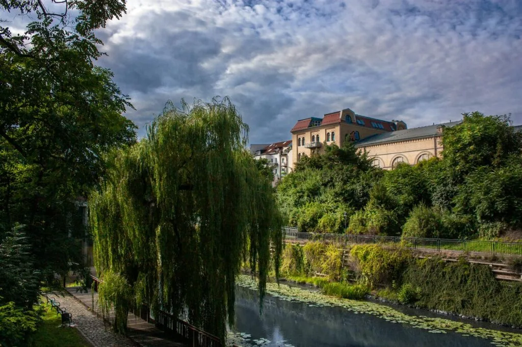 Beautiful riverside view in Leipzig, Germany, with lush greenery and dramatic cloudy sky.